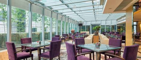 A spacious indoor area with glass walls, tables, and purple chairs.