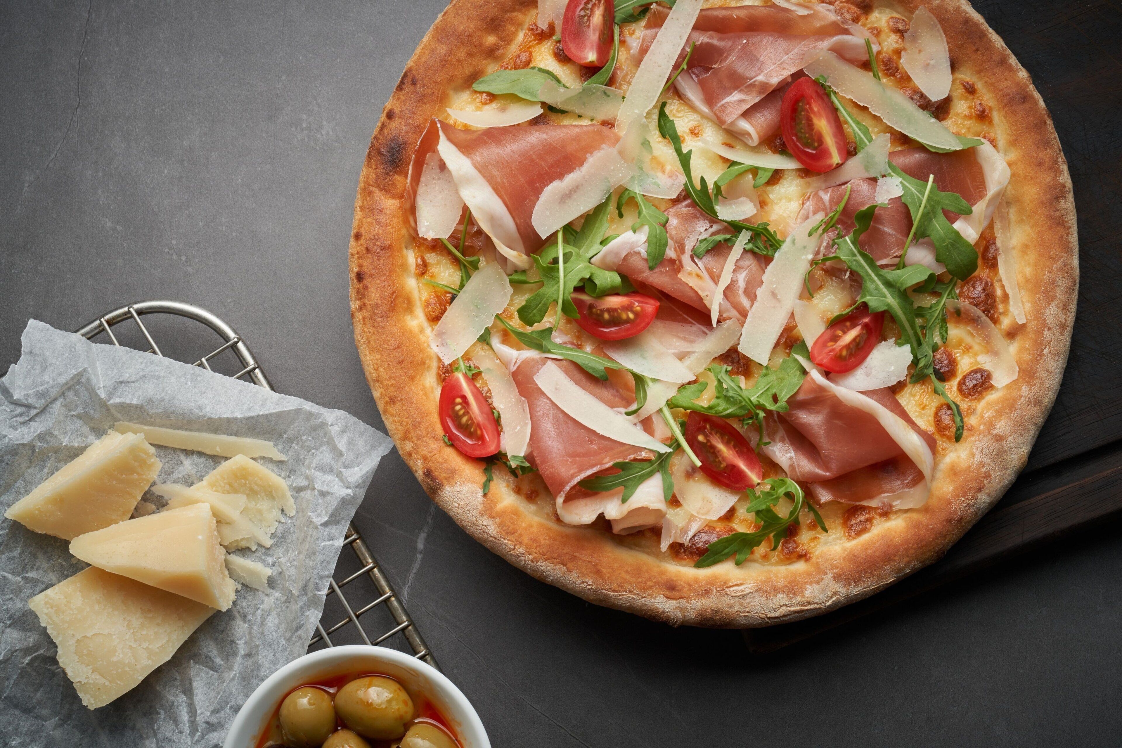 A pizza with toppings and a bowl of olives on a dark surface.