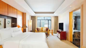 A hotel room with a large bed, a sofa, a TV, and a view of the city.