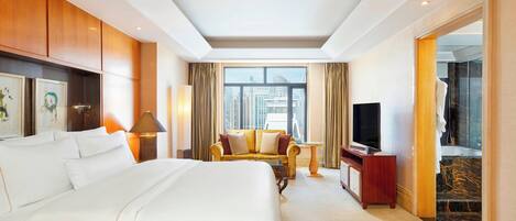 A hotel room with a large bed, a sofa, a TV, and a view of the city.