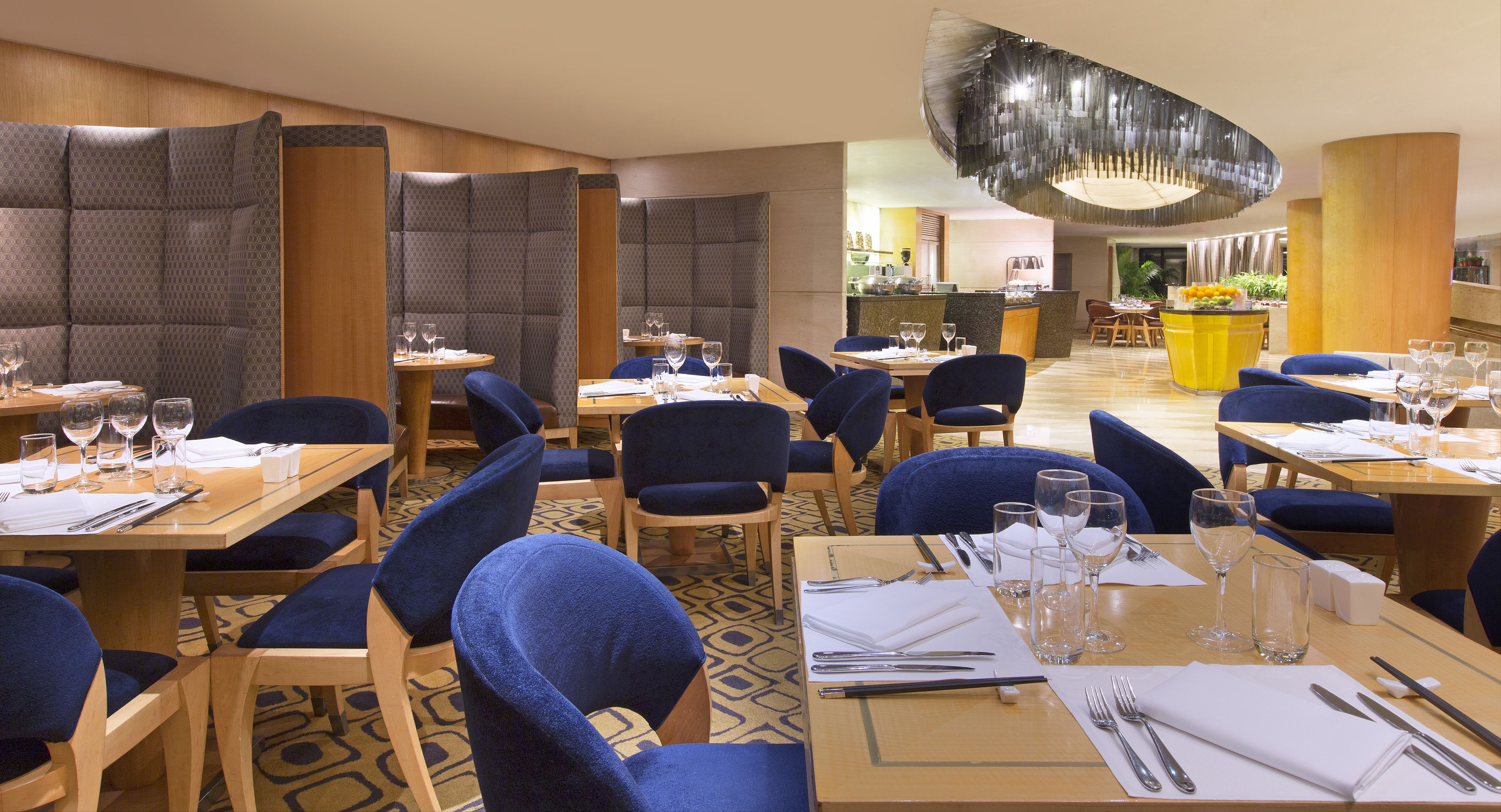 A modern restaurant with blue upholstered chairs, wooden tables, and a central bar area.