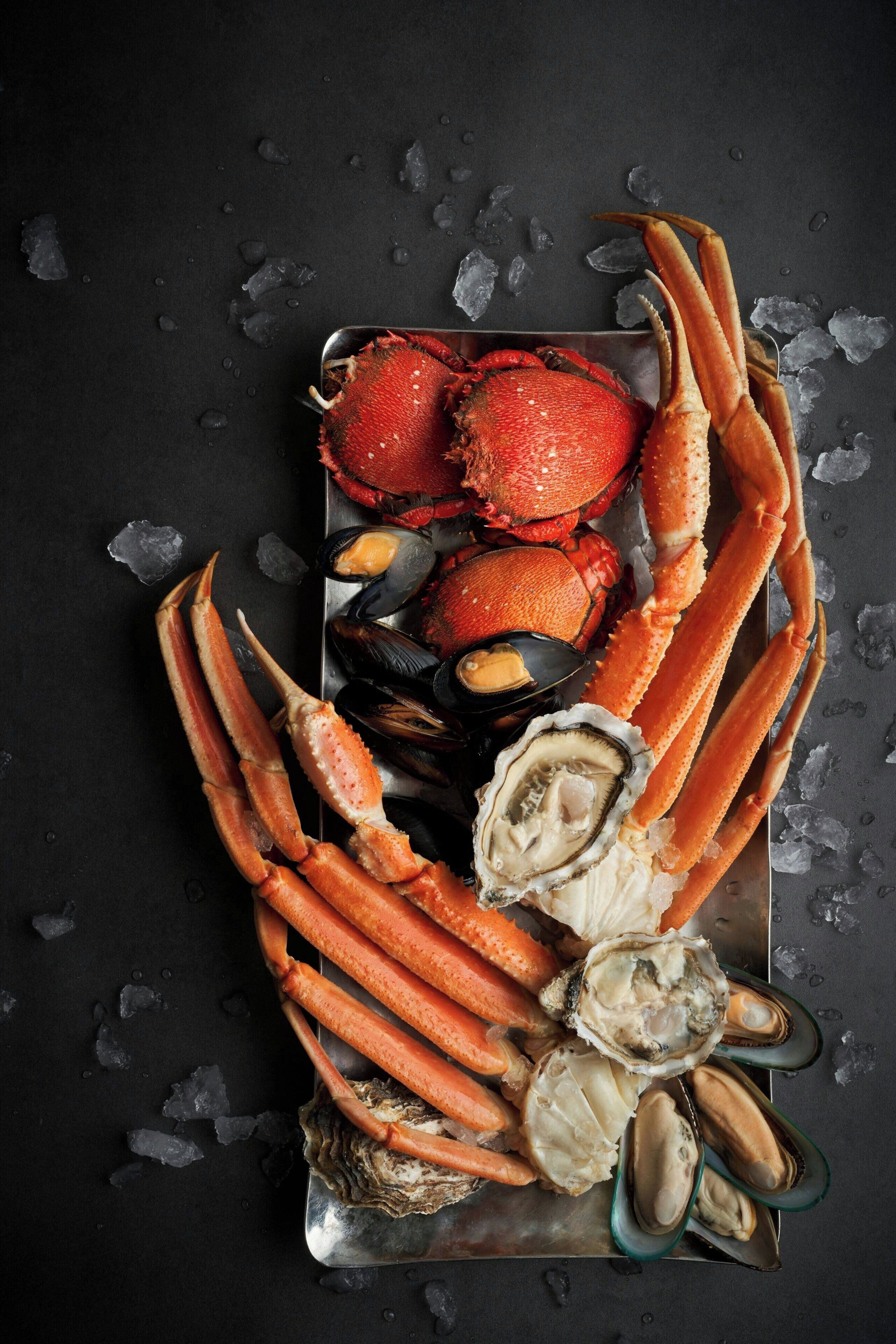 Un plateau de fruits de mer comprenant des pinces de crabe, des moules et des huîtres, présenté sur un plateau en métal avec de la glace.