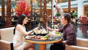 A couple dining at a table with a seafood platter, wine glasses, and a dessert selection in a modern indoor setting with palm trees and a view of a building. - The Westin Bund Center, Shanghai (Shanghai)