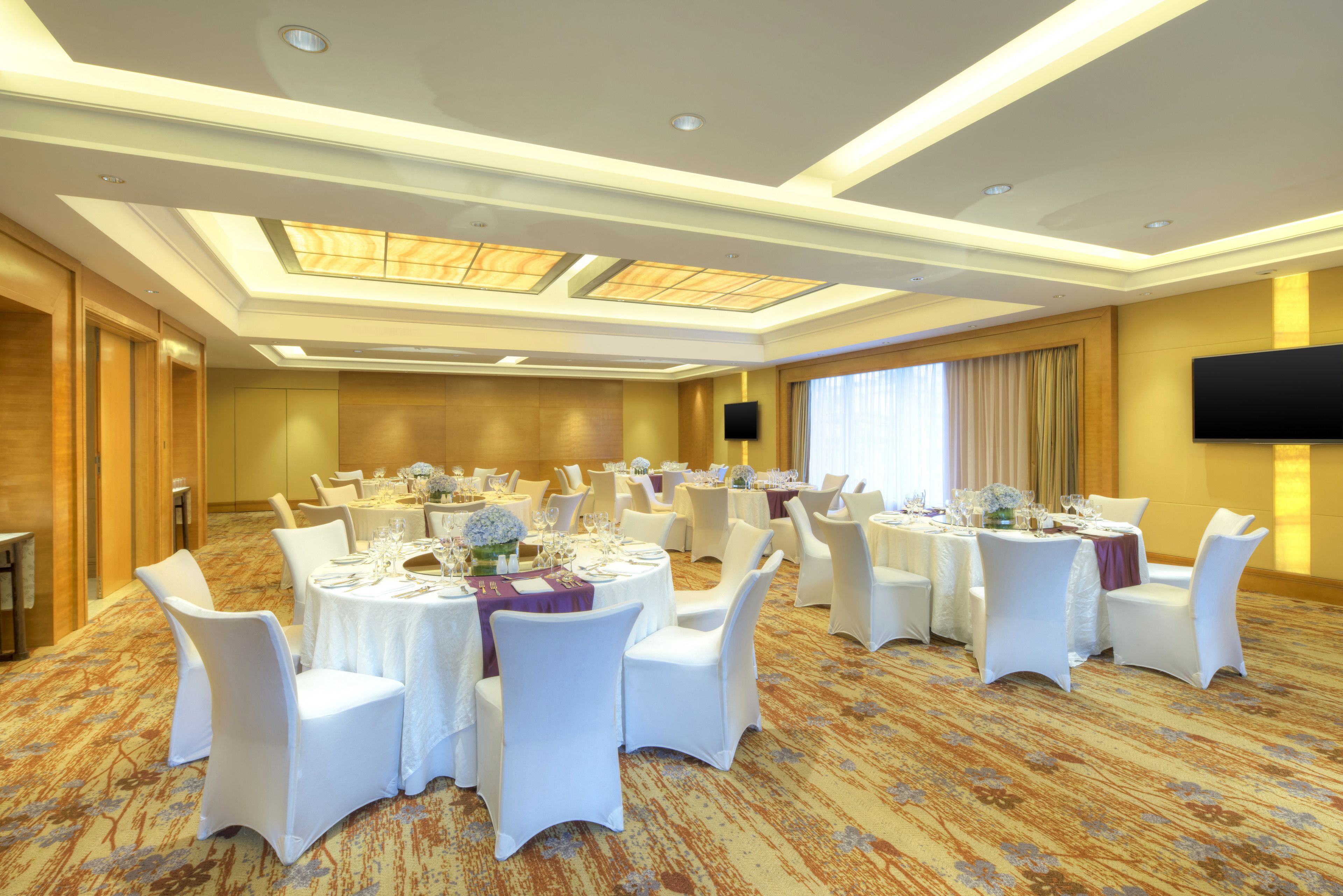 Un salón de banquetes con mesas redondas, sillas blancas y suelo alfombrado.