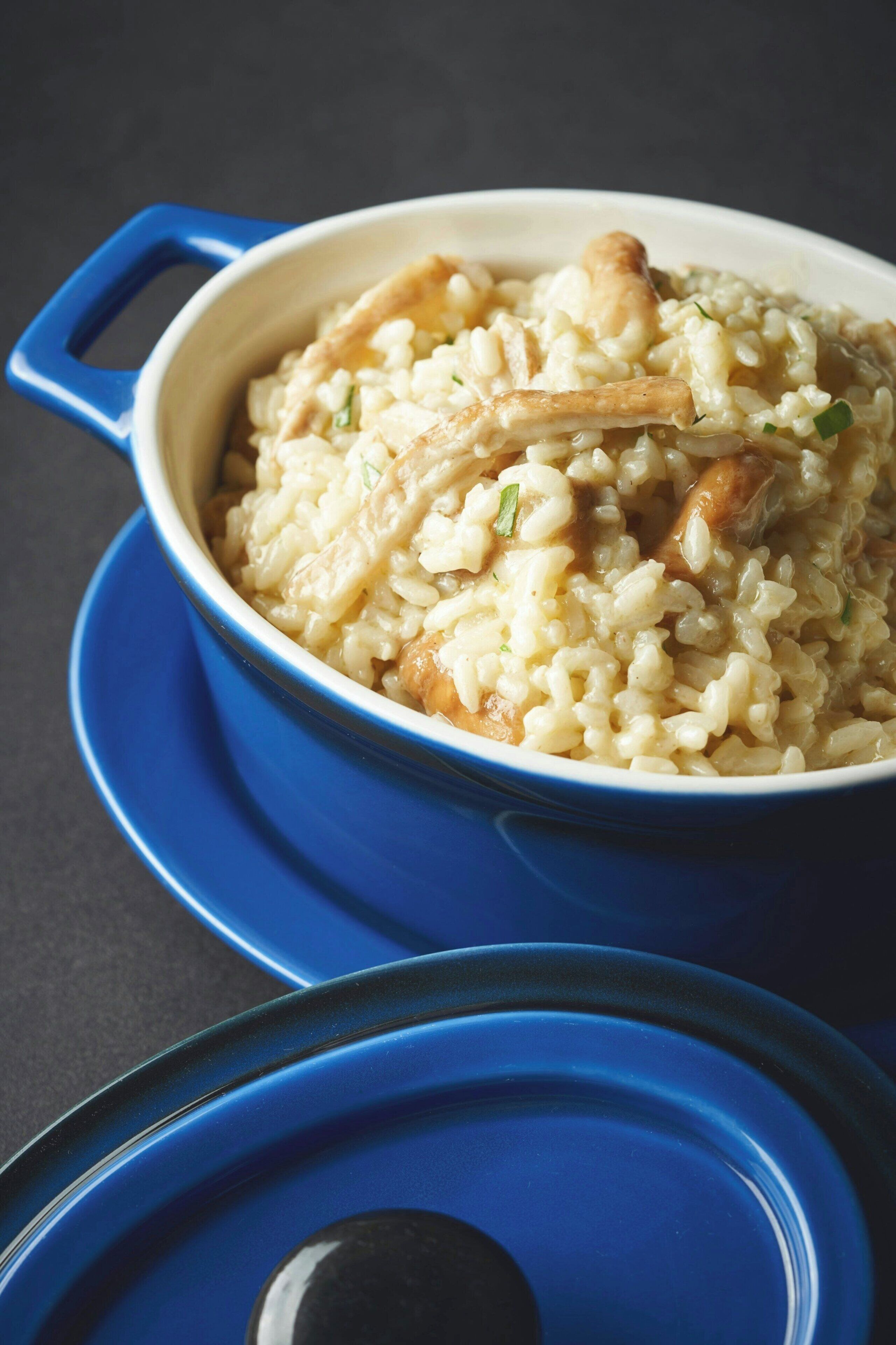 A blue pot filled with rice and chicken on a dark surface.