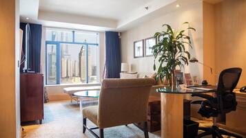 Hotellihuone, jossa on suuri ikkuna, työpöytä, tuoli, viherkasvi ja sänky.