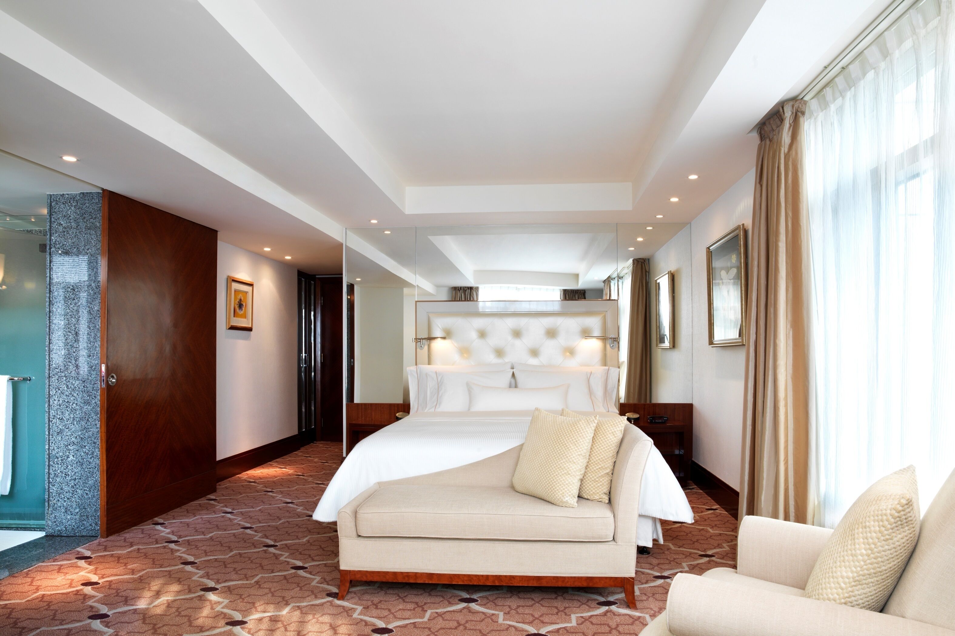 A hotel room with a large bed, a sofa, a mirror, and a carpeted floor.