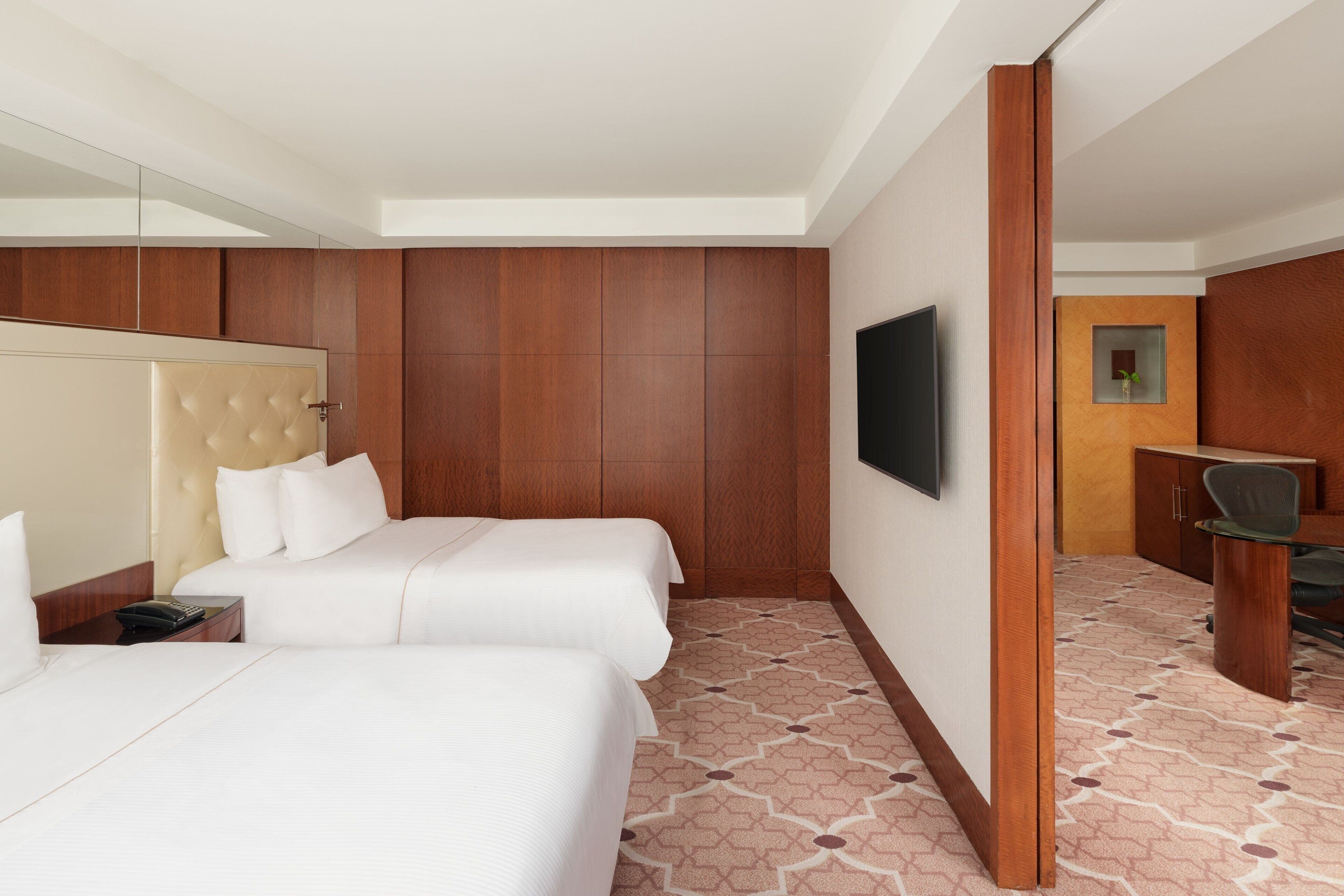 A hotel room with two beds, a television, a desk, and a chair.