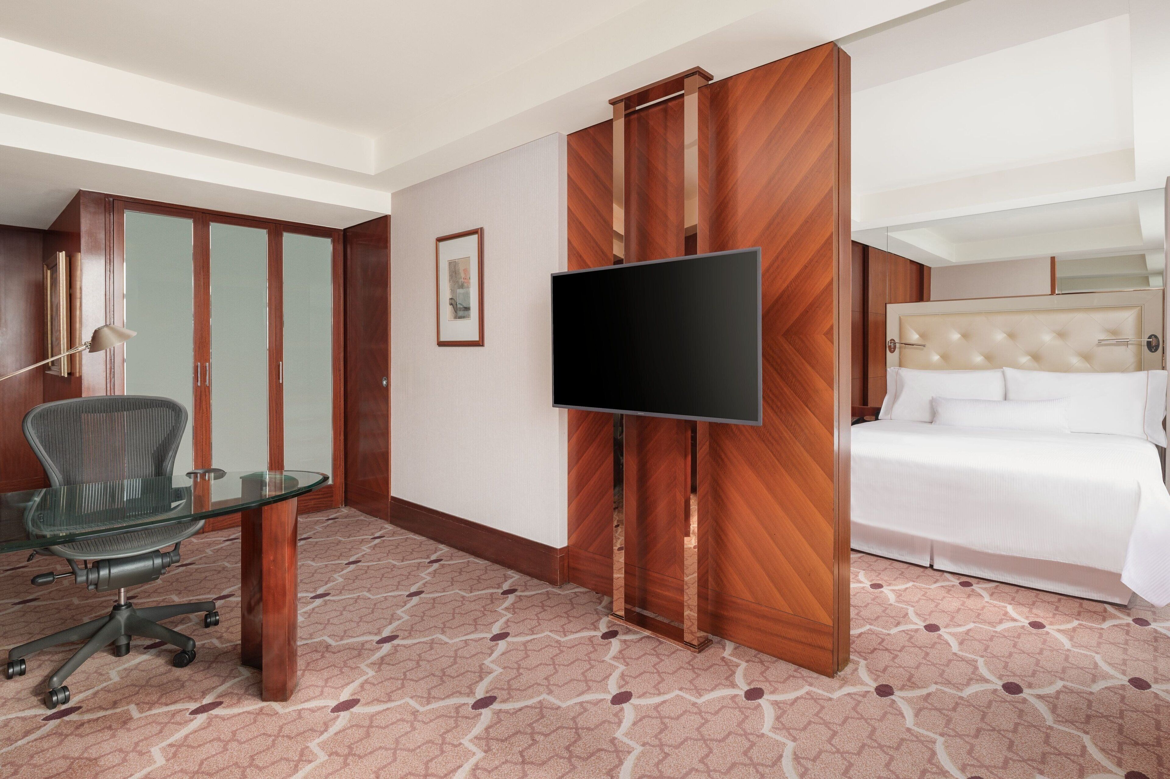 A hotel room with a bed, a TV, a desk with a chair, and a wardrobe.
