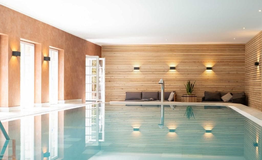 Una piscina con un muro de madera, un espacio de estar con cojines y una escalera.