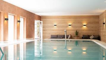Una piscina con un muro de madera, un espacio de estar con cojines y una escalera.
