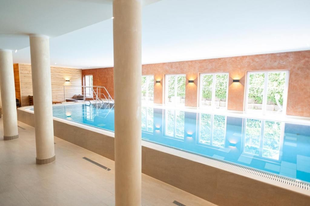 Una piscina interior con agua cristalina, rodeada de columnas y un muro de madera.
