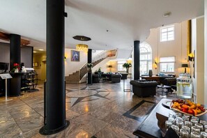A spacious lobby with a grand staircase, a reception desk, and a seating area with a fruit basket and glasses. - Bernstein Schlosshotel Ballenstedt (Ballenstedt)