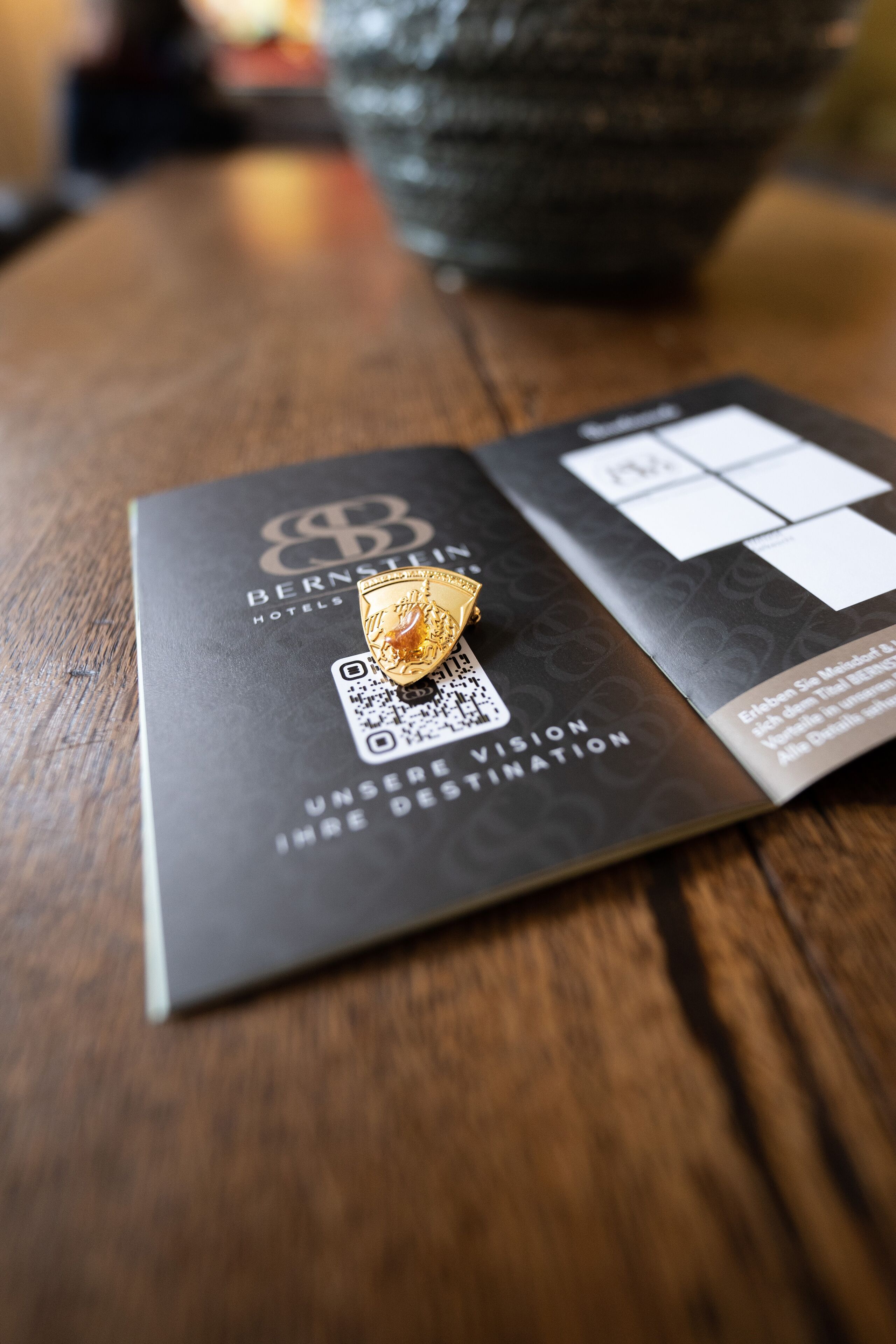Un folleto con un código QR y un emblema dorado sobre una superficie de madera.