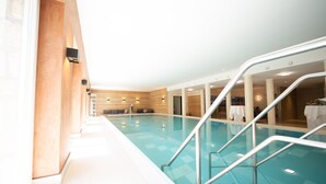 Una piscina interior con agua cristalina, rodeada por un suelo de baldosas blancas y una pared de madera.