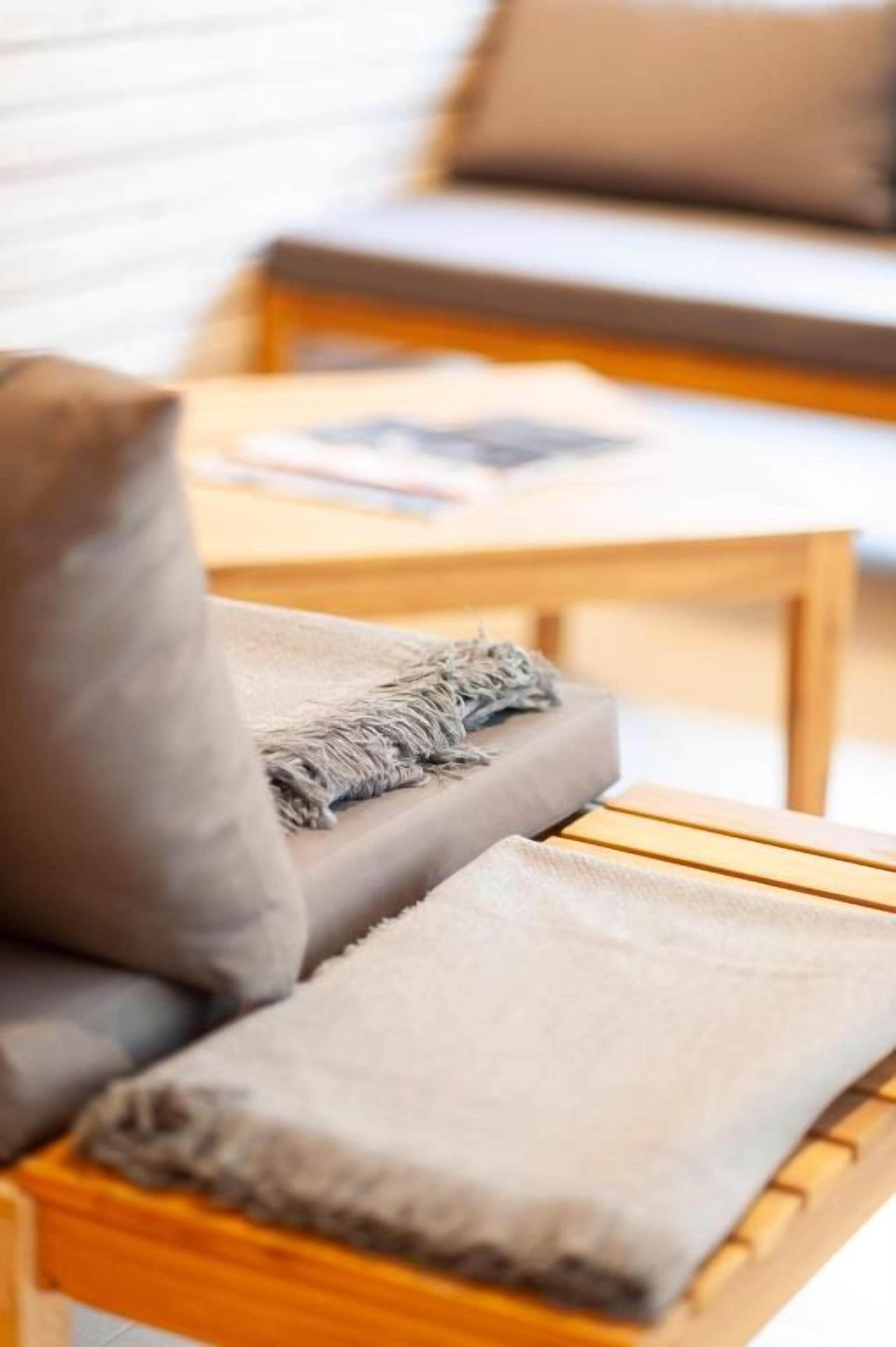 A wooden bench with a cushion and a blanket.