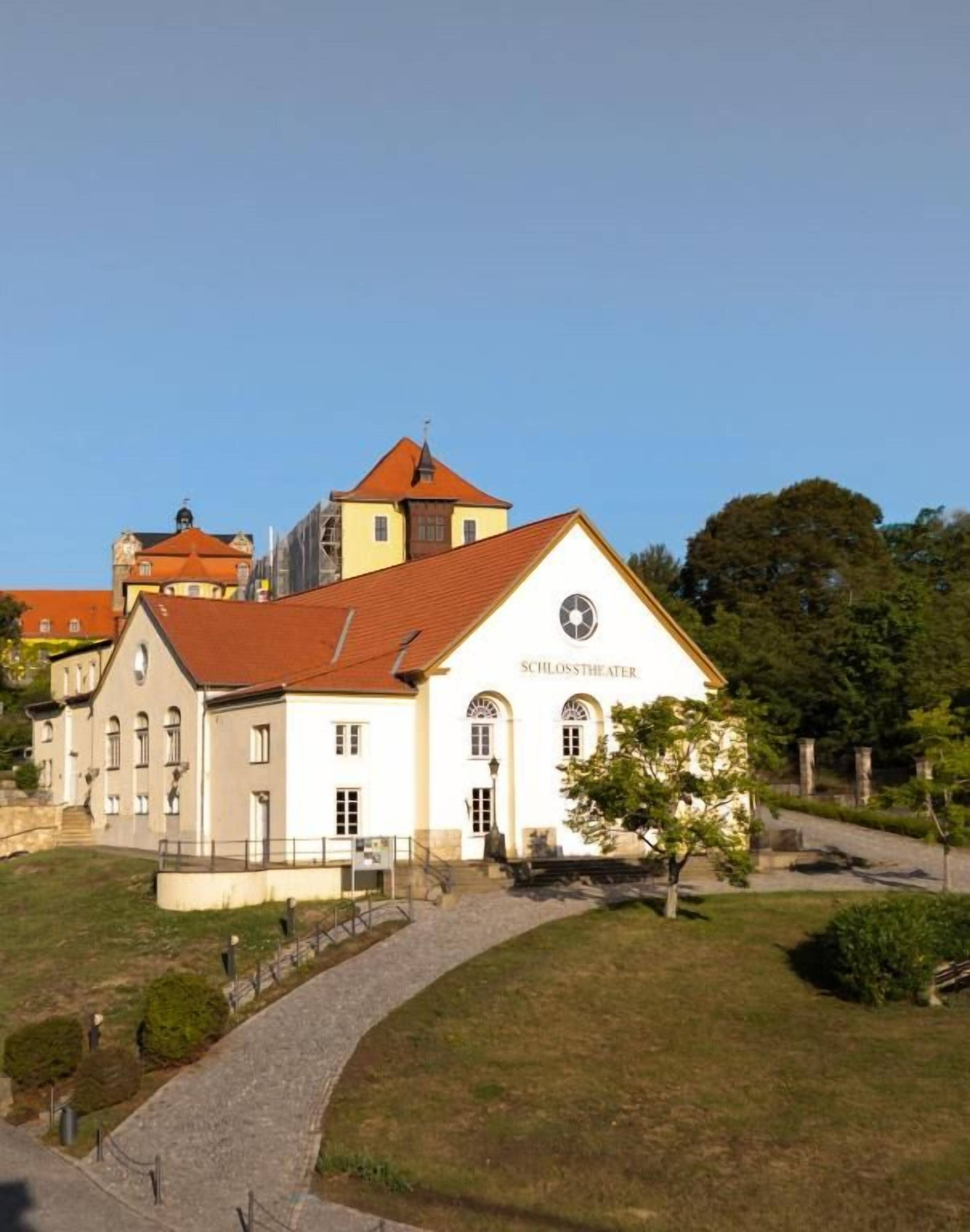 Un bâtiment sur lequel on peut lire l’inscription « SCHLOSSTHEATER », et un chemin pavé qui y mène.