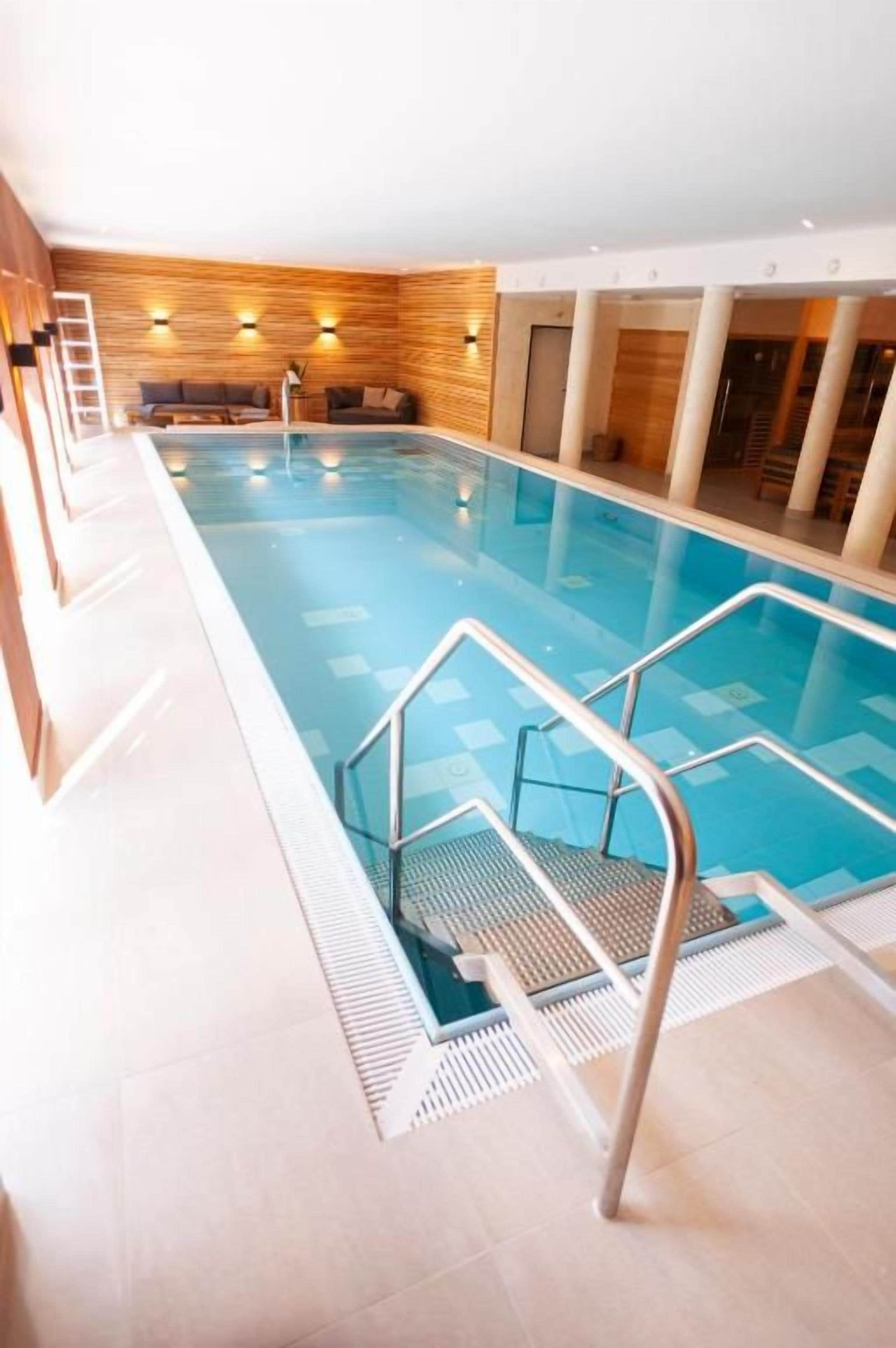 Ein Innenpool mit einer Holzverkleidung, einer Sitzecke und einer Treppe, die zum Pool führt.
