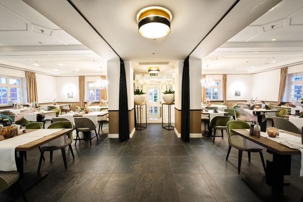 Ein geräumiges Restaurant mit mehreren Tischen, Stühlen und einem zentralen Gang, darüber ein Kronleuchter.