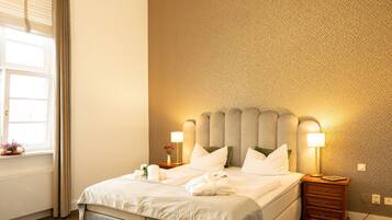 A hotel room with a bed, bedside lamps, a nightstand, and a window with curtains.