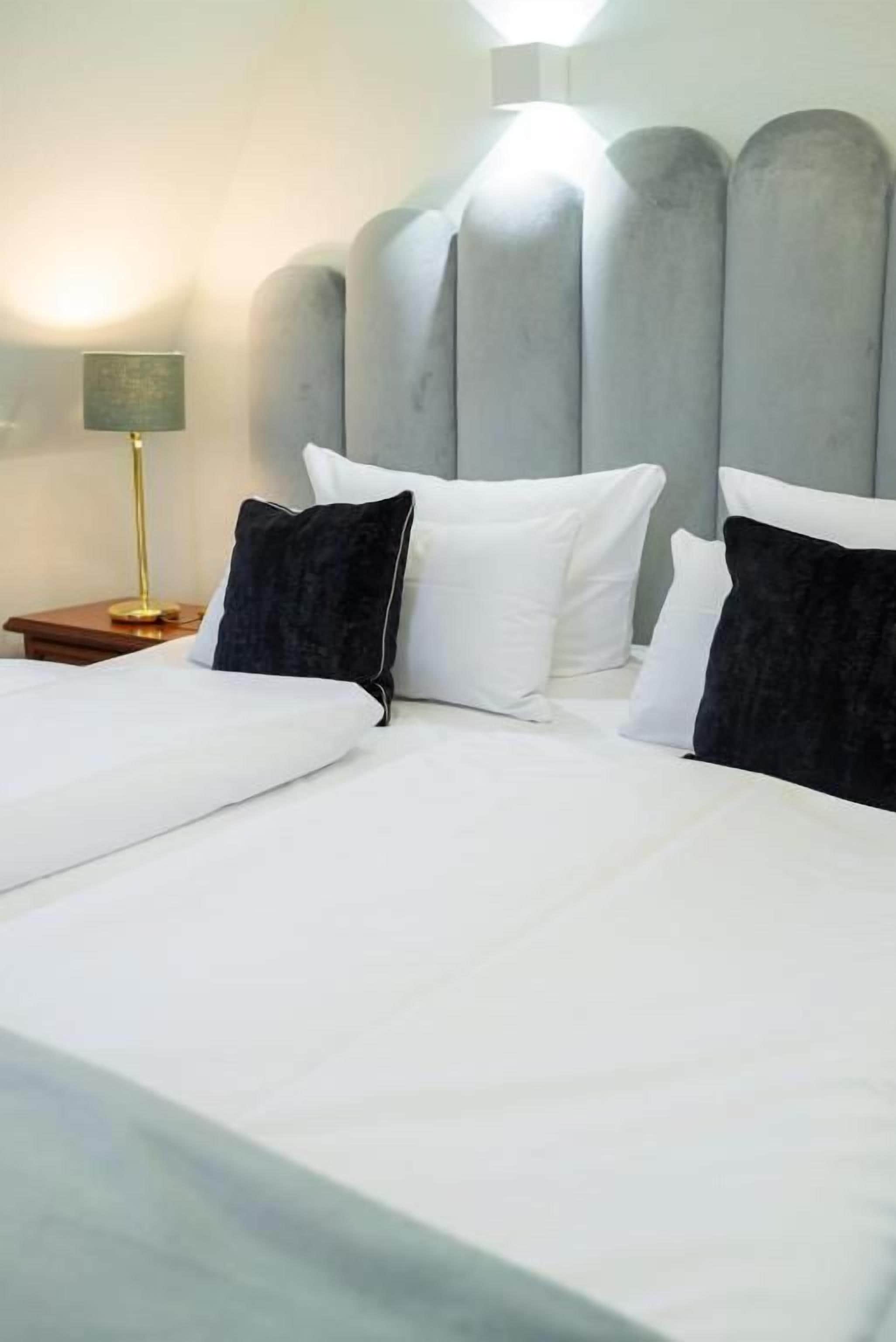 A hotel room with a large bed, a nightstand with a lamp, and a headboard with built-in lighting.