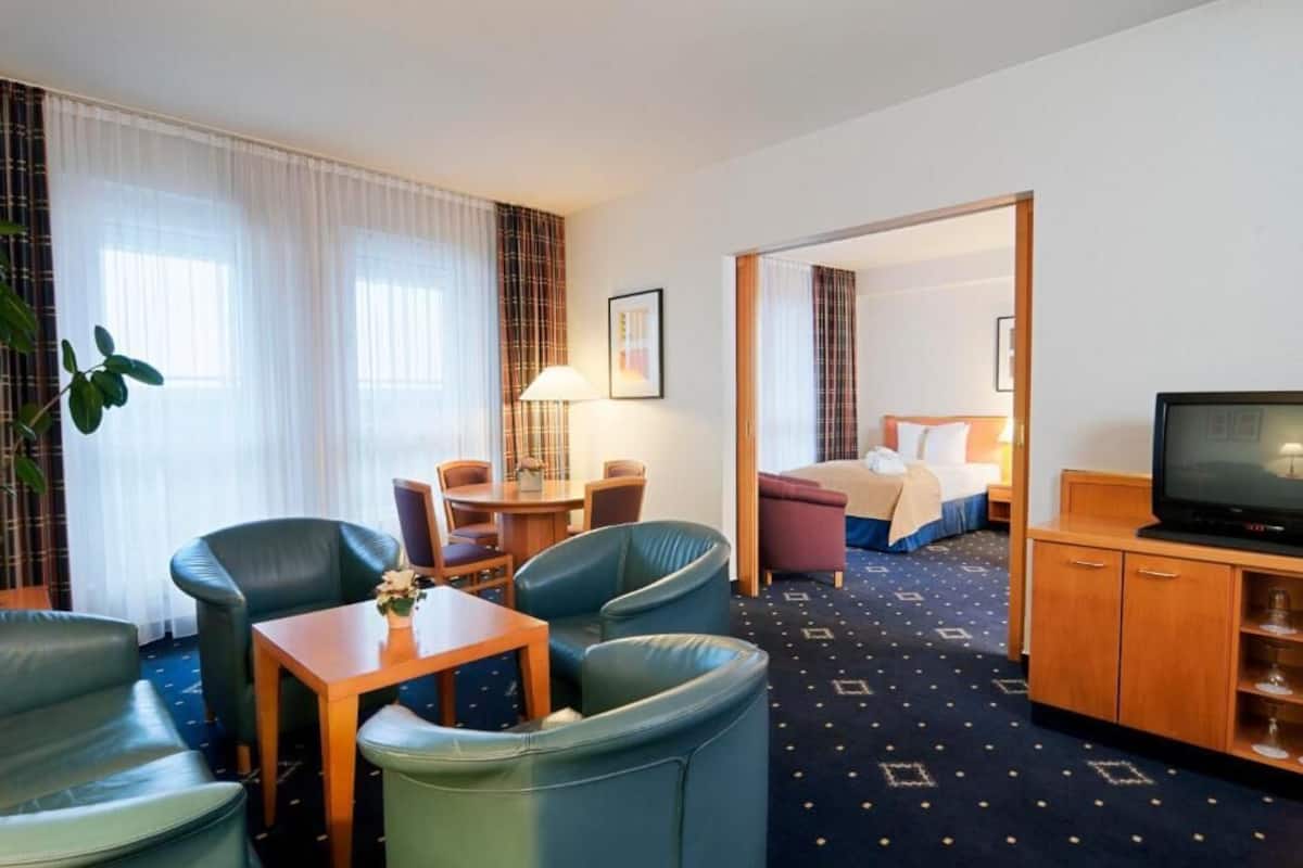 Une chambre d’hôtel comprenant un lit, une télévision, un bureau avec une lampe et un coin salon avec des fauteuils et une table.