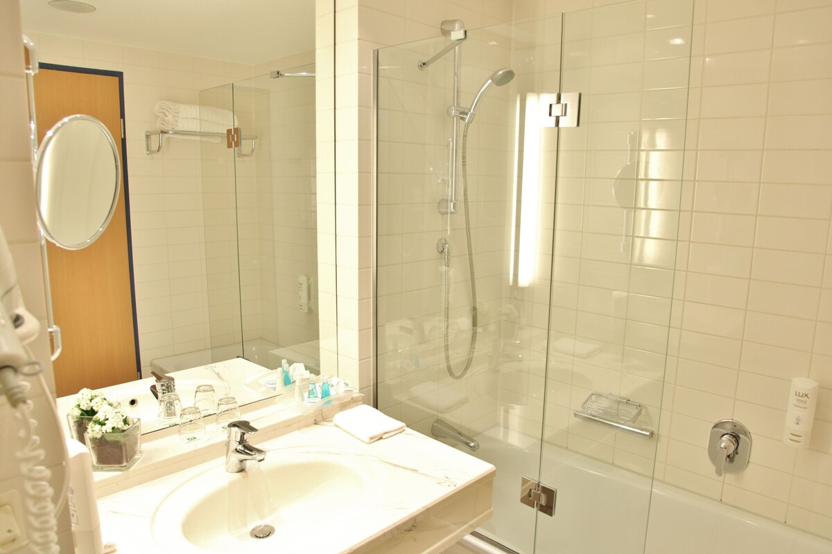 A modern bathroom with a glass-enclosed shower, a large mirror, and a vanity with toiletries.