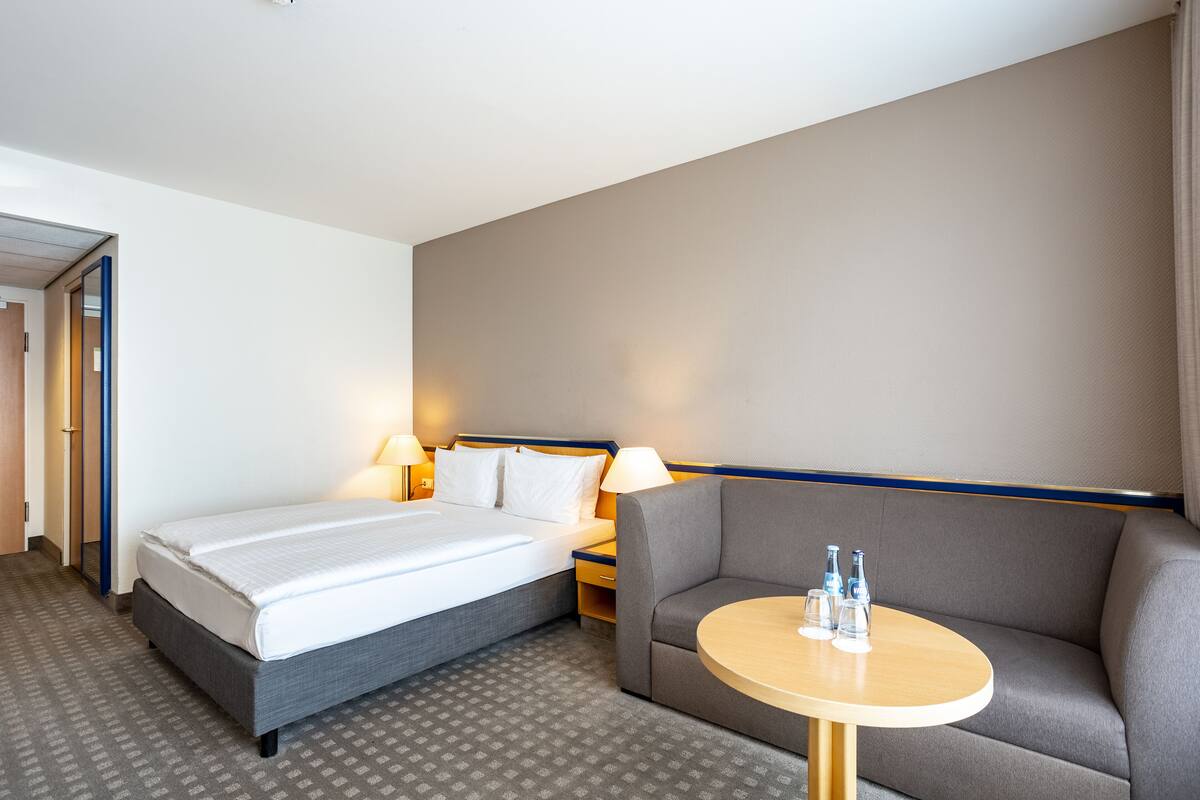 Une chambre d’hôtel avec un lit, un canapé, une petite table et une table de chevet avec des lampes.