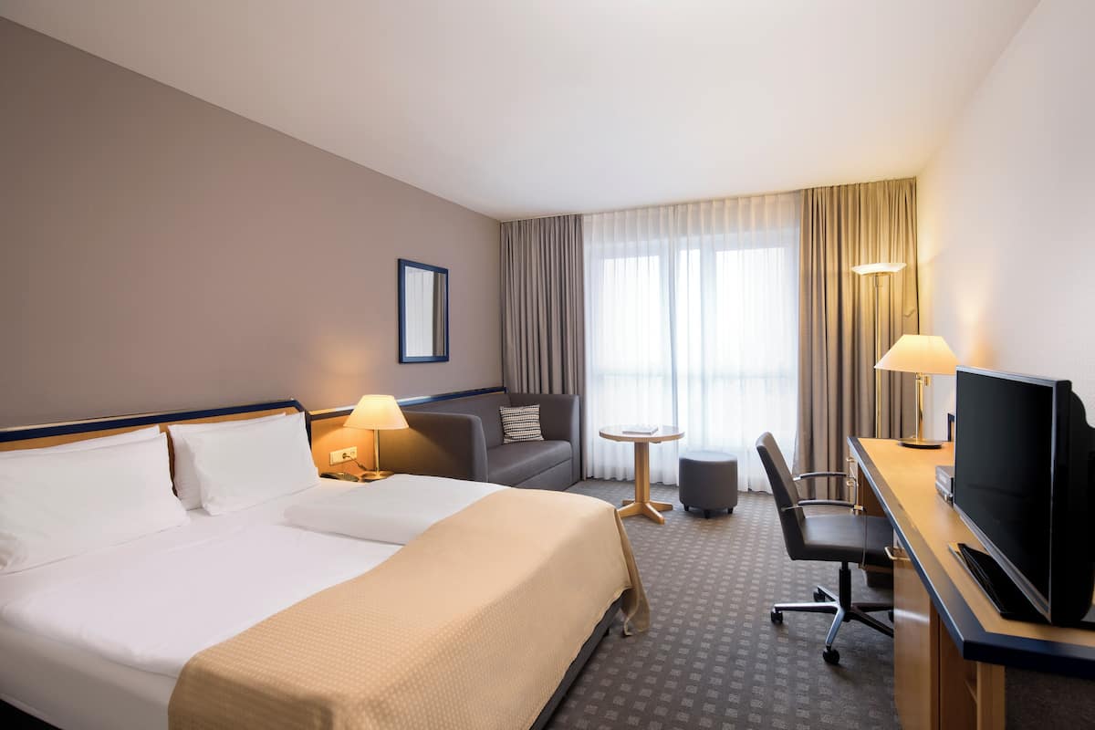 Une chambre d’hôtel avec un grand lit, un bureau avec une télévision, une petite table et un canapé.