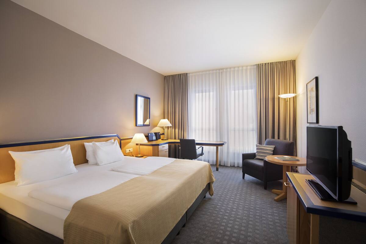 Une chambre d’hôtel avec un grand lit, un bureau avec une chaise, une télévision et une petite table.