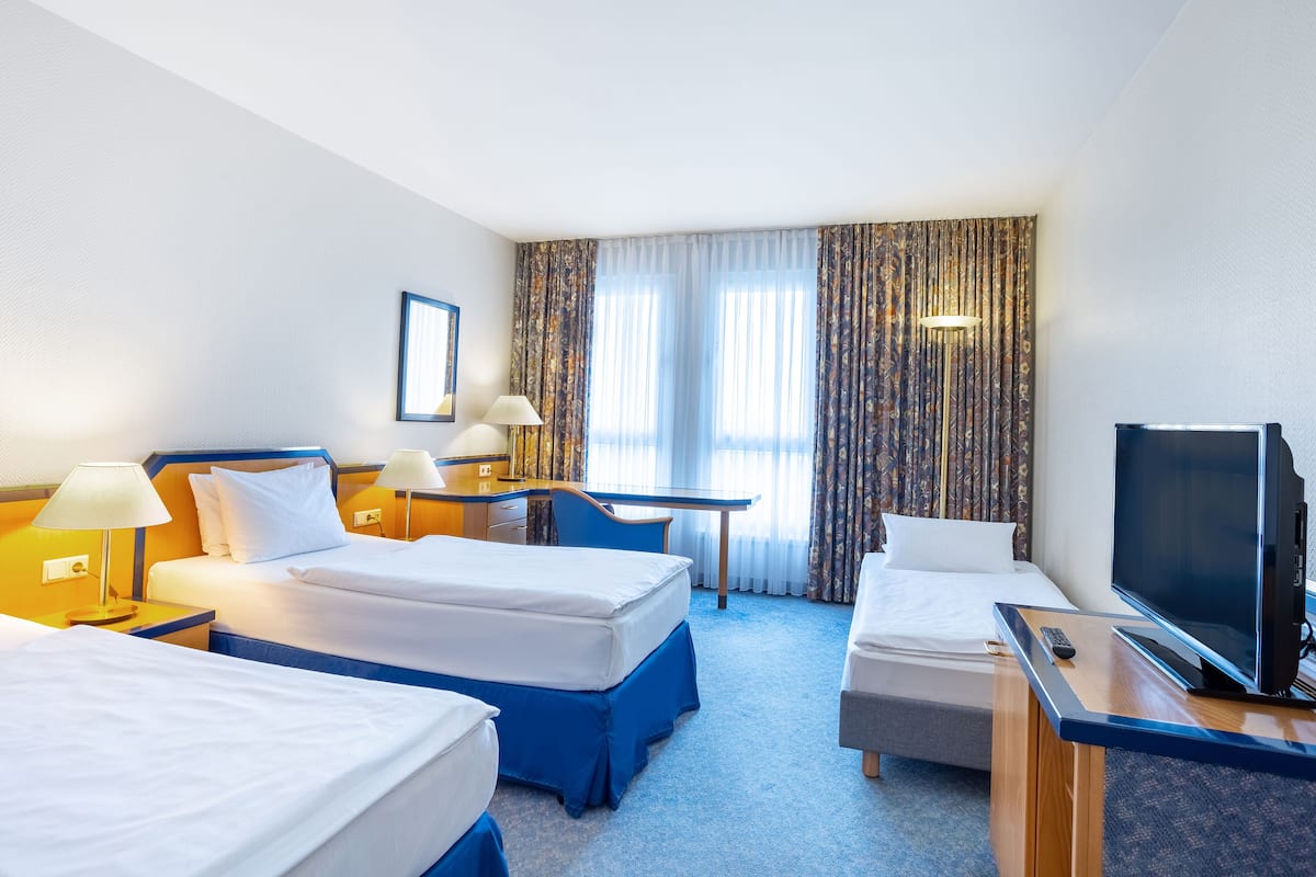 Une chambre d’hôtel avec deux lits simples, un bureau, une télévision et une grande fenêtre avec des rideaux.