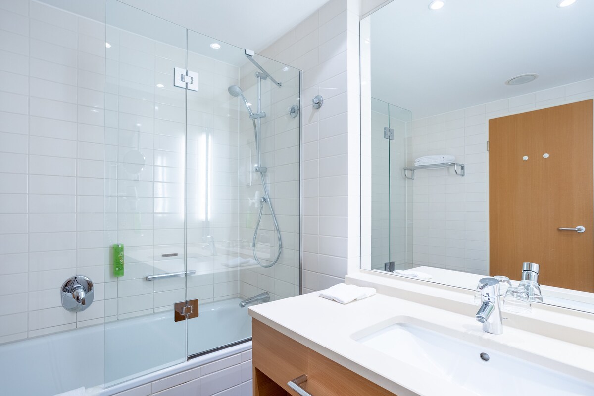 Un baño moderno con cabina de ducha de vidrio, un lavabo blanco con espejo y un mueble de tocador de madera.