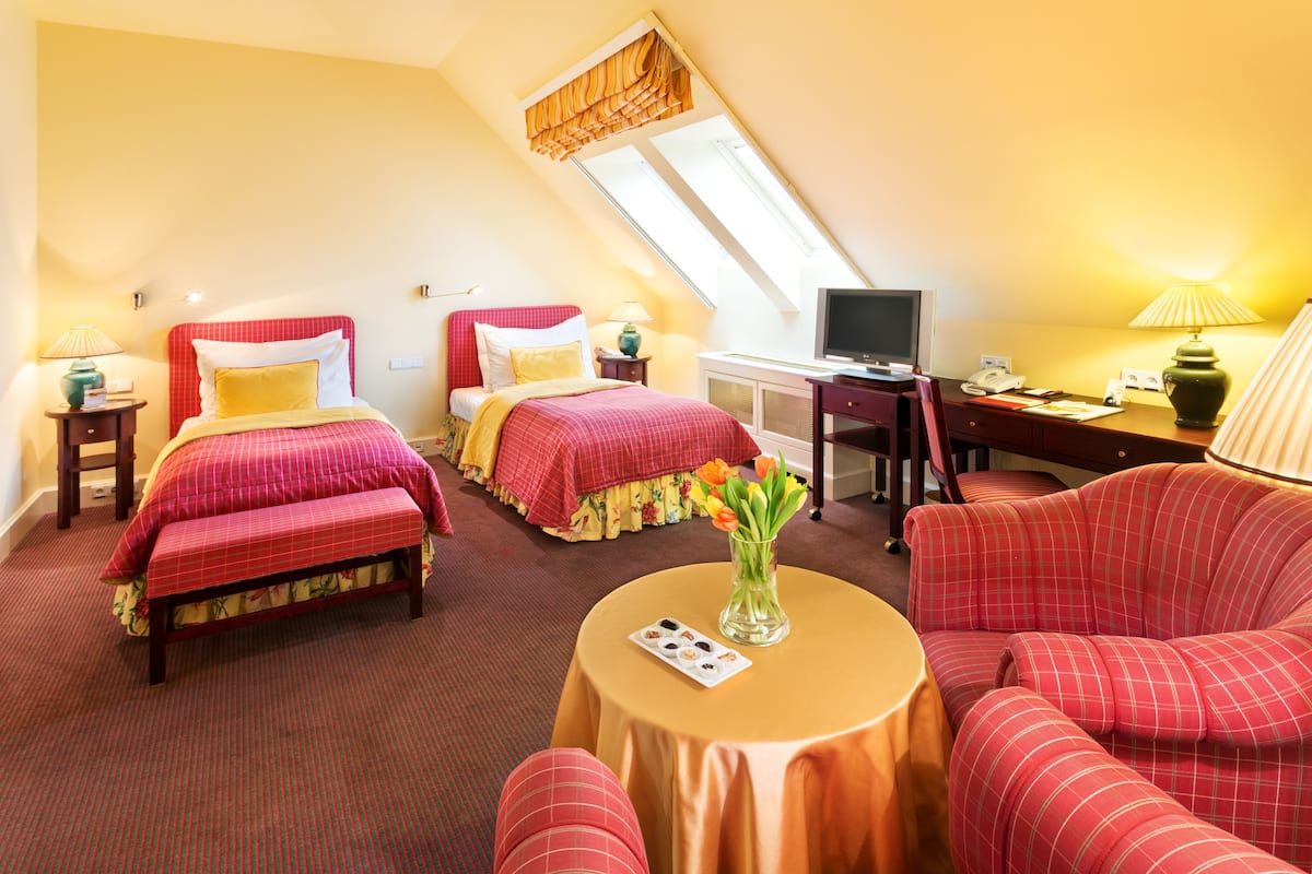 A hotel room with two beds, a desk, a chair, a television, and a small table with a vase of flowers.