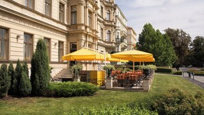 Un patio de hotel con mobiliario exterior y un edificio grande de arquitectura clásica.