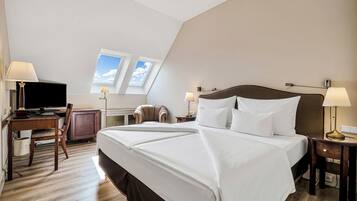 A hotel room with a large bed, a desk with a computer, a chair, a lamp, and a television.