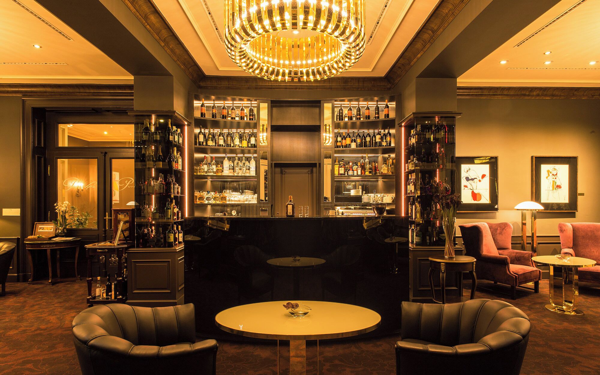 A bar area with a round table, leather chairs, and a chandelier.