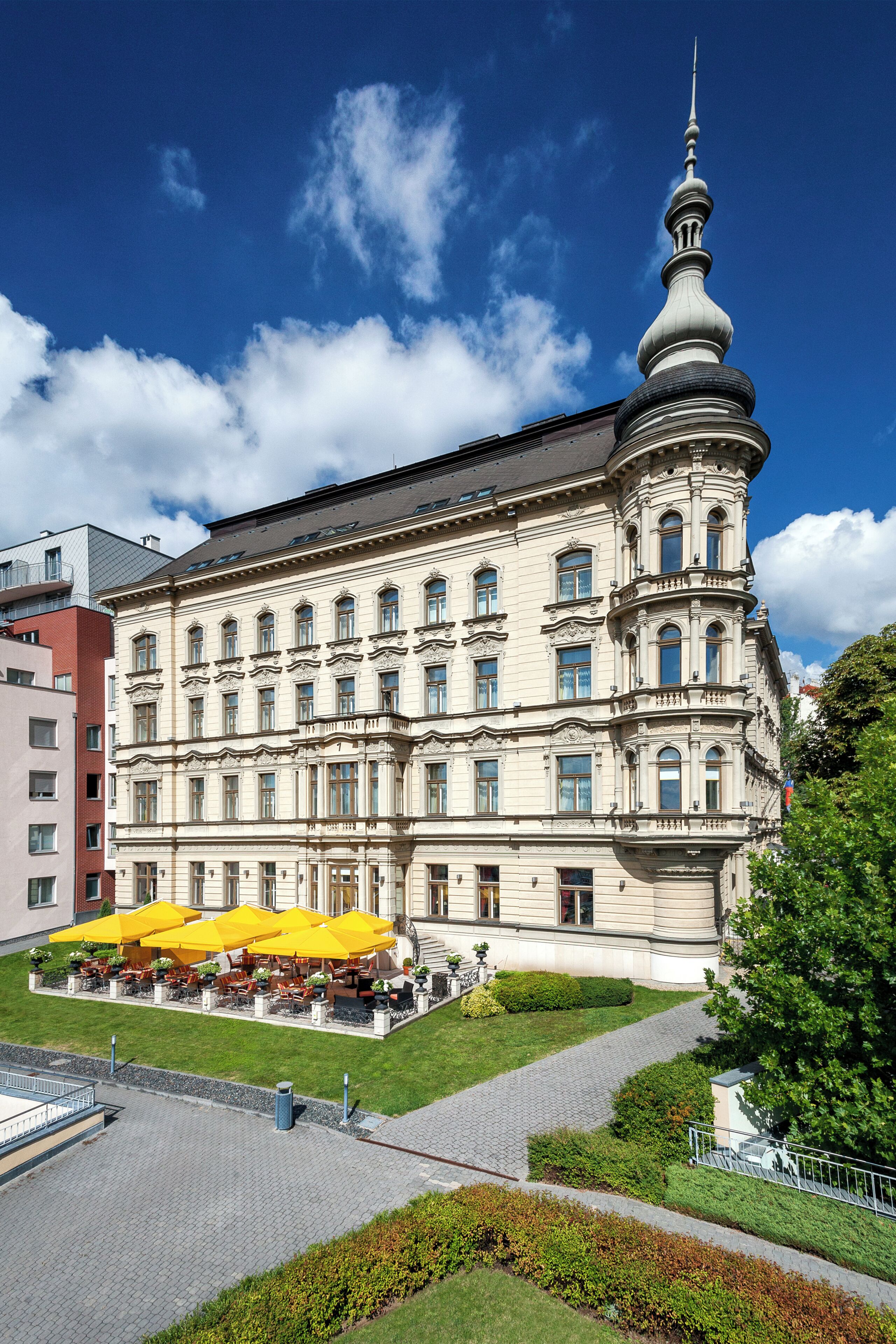 A historic building with a prominent tower, a courtyard with yellow umbrellas, and a well-maintained garden.