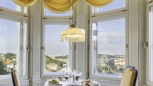 Comedor con una mesa dispuesta para dos personas, ventanas amplias con cortinas y una araña.