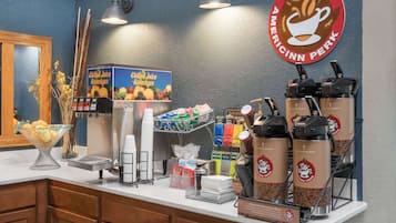A coffee station with a coffee machine, a box of chilled juice beverages, and a sign for Americinn Perk.