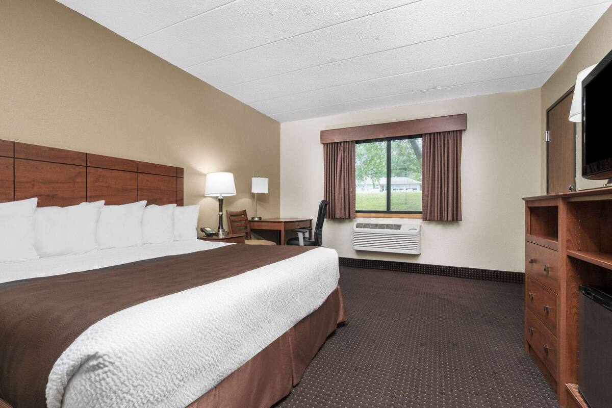 A hotel room with a large bed, a desk, a chair, a television, and a window with curtains.