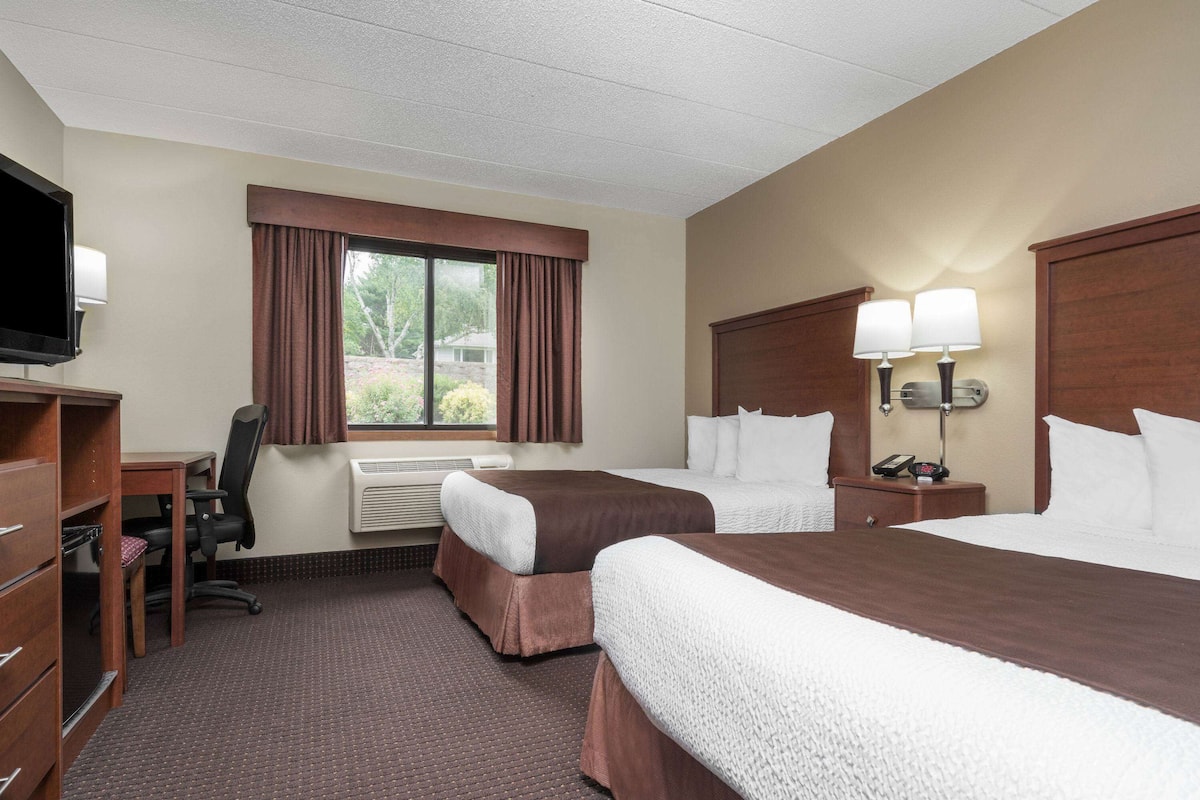 A hotel room with two beds, a desk, a chair, a TV, and a window with curtains.