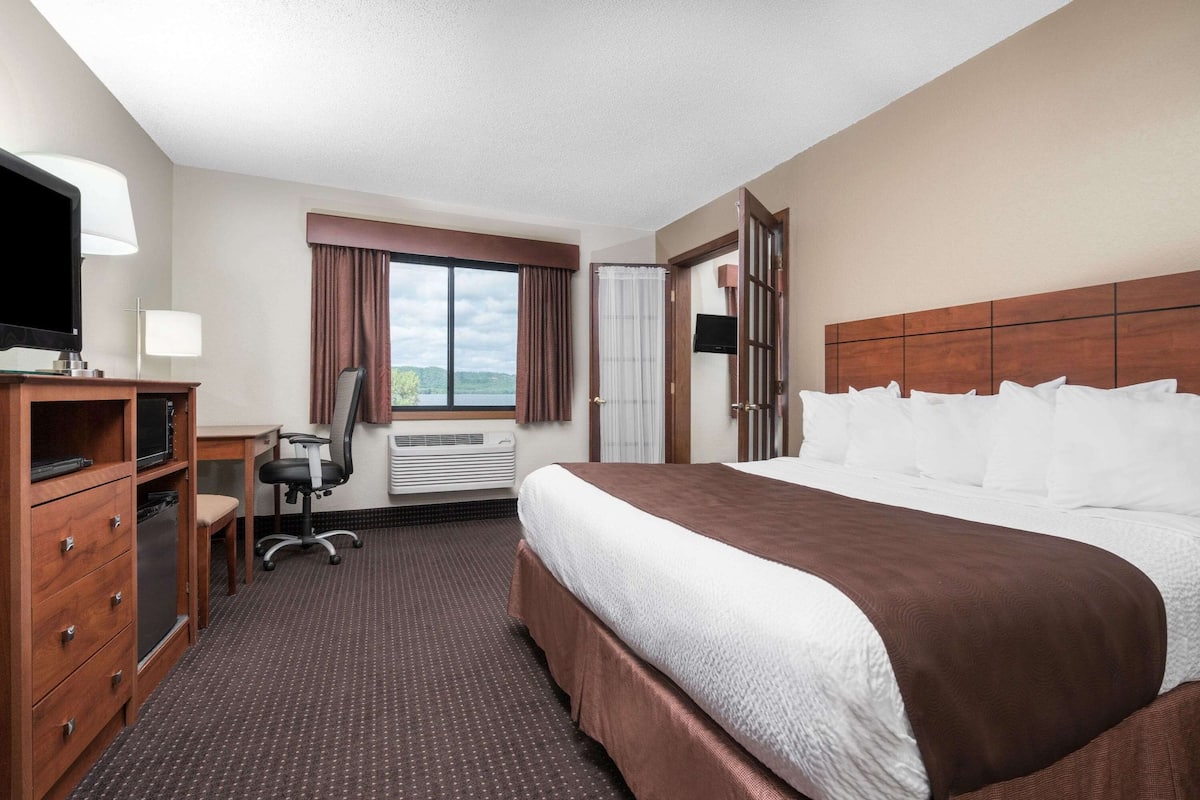 A hotel room with a large bed, a desk with a chair, a television, and a window with curtains.