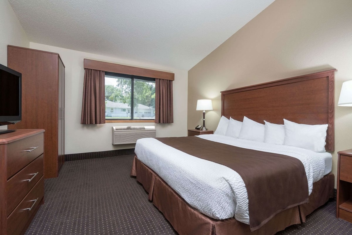 A hotel room with a large bed, a television, a desk, and a window with curtains.