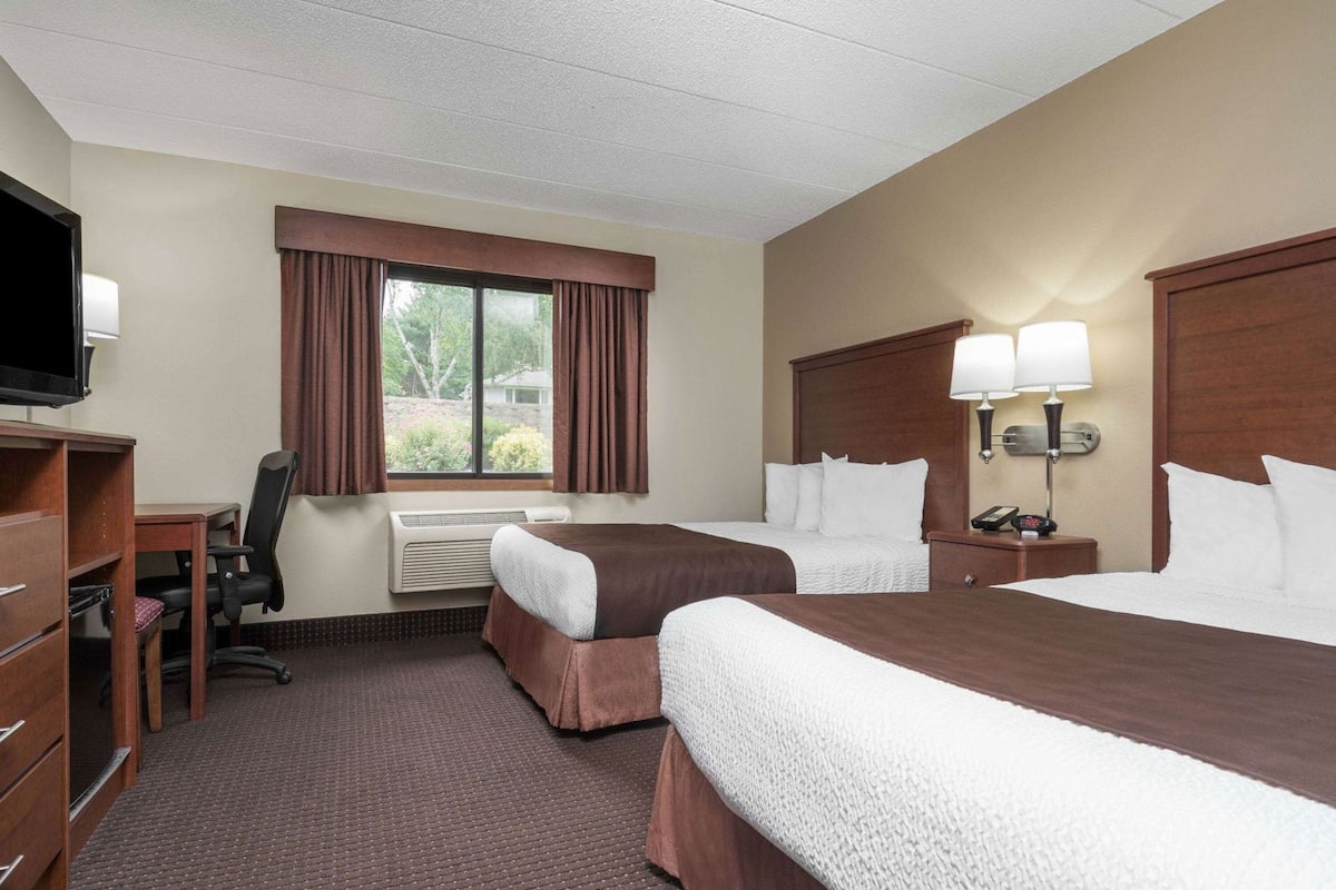 A hotel room with two beds, a desk, a chair, a TV, and a window with curtains.