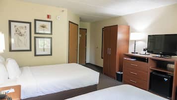 A hotel room with two beds, a desk with a TV, a lamp, and framed pictures on the wall.