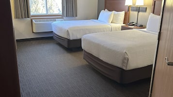 Una habitación de hotel con dos camas, una ventana con cortinas, un calentador fijado a la pared y una mesita de noche con lámpara.