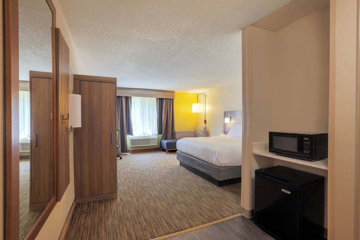 A hotel room with a bed, a desk, a microwave, and a refrigerator.