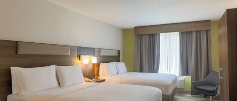 Quarto de hotel com duas camas, uma escrivaninha, uma cadeira e uma janela grande com cortinas.