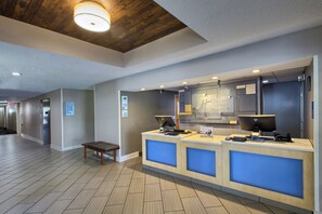 A hotel reception area with a wooden ceiling, a reception desk with a computer and a phone, and directional signs for hotel amenities.