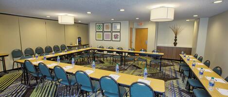 A conference room with a long table, chairs, water bottles, and framed pictures on the wall.
